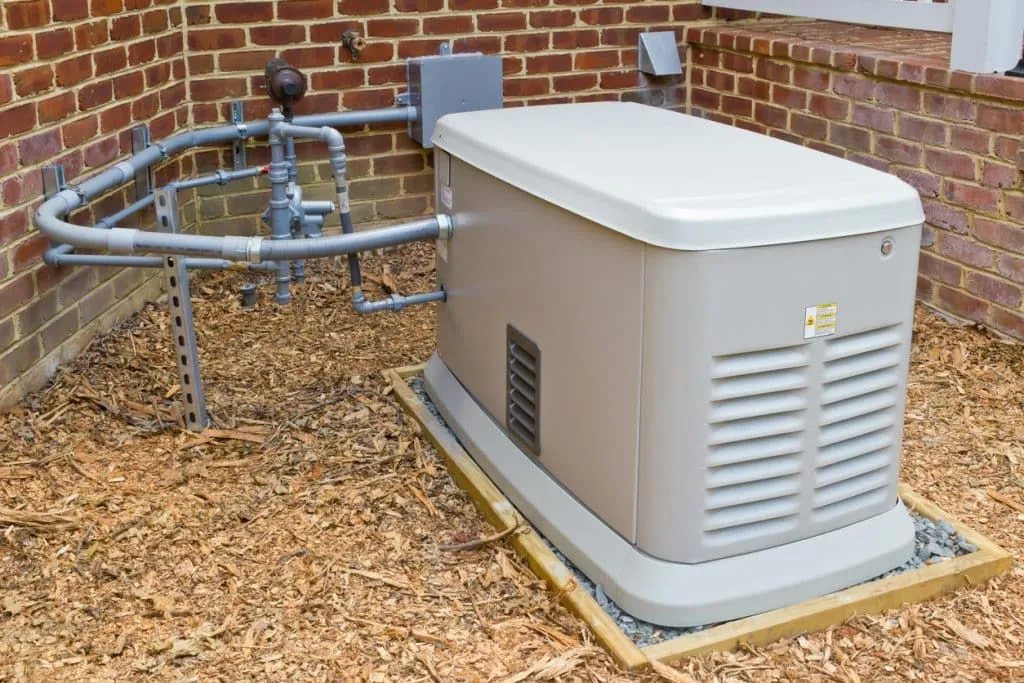 A generator is sitting on the ground next to a brick wall.