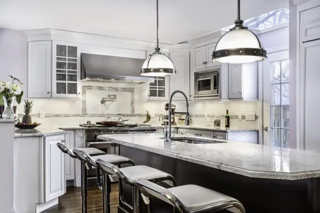 A kitchen with white cabinets, stainless steel appliances, a large island and stools.