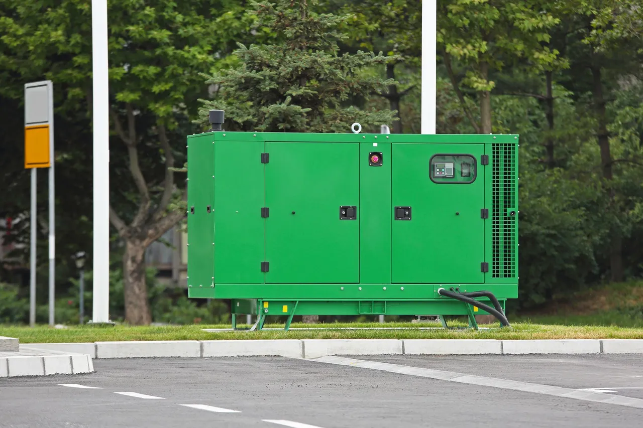 Green industrial generator on a grassy area, next to a road and trees. Green industrial generator on a grassy area, next to a road and trees.