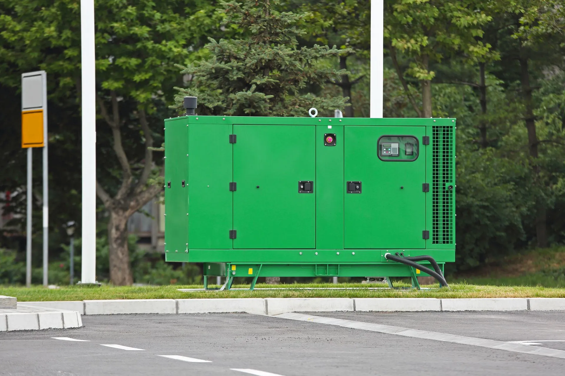 Green industrial generator on a grassy area, next to a road and trees. Green industrial generator on a grassy area, next to a road and trees.