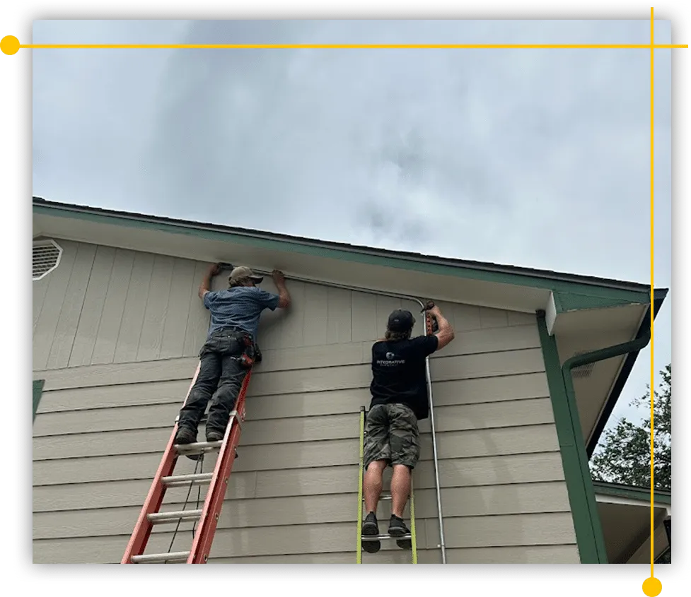 Two men are working on the side of a house on a ladder. Two men are working on the side of a house on a ladder.