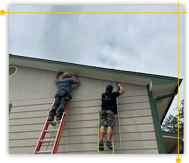 Two men are working on the side of a house on a ladder. Two men are working on the side of a house on a ladder.